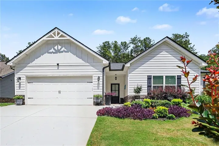 Exterior featuring white siding, a prominent front garden with varied plantings, a two-car garage, dark window shutters, and a covered front entry