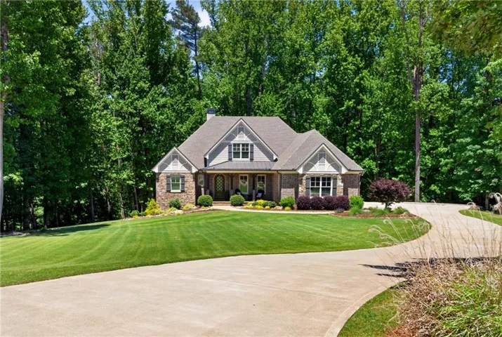 Traditional-style residence featuring a prominent front gable, a stone and siding exterior, a manicured lawn, a winding driveway, and mature perimeter trees