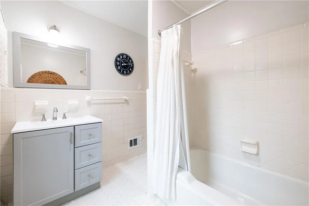 Full bathroom featuring vanity, shower / bath combination with curtain, tile walls, a wainscoted wall, and light tile patterned floors