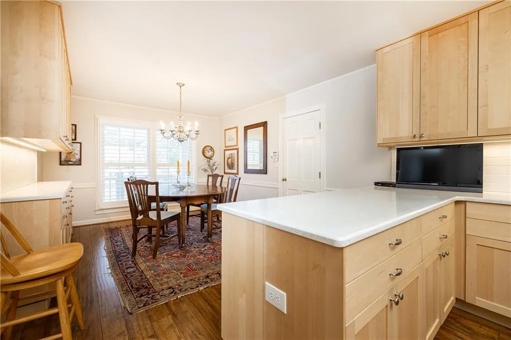Kitchen with light brown cabinets, crown molding, dark wood-style flooring, pendant lighting, and a peninsula
