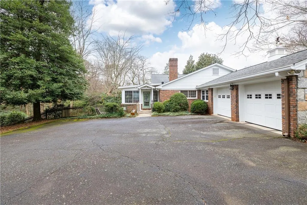View of side of property featuring driveway, a chimney, an attached garage, and a shingled roof