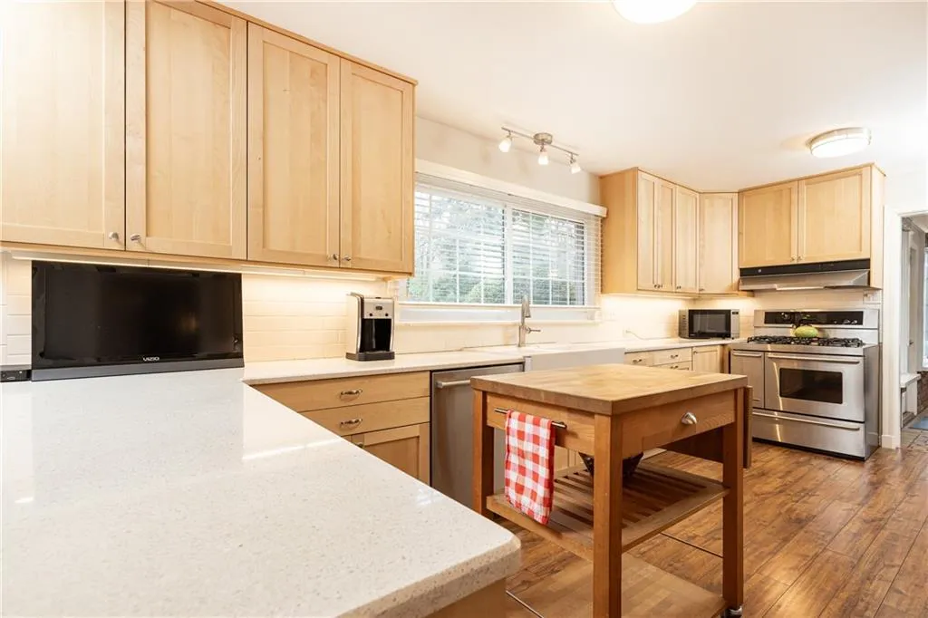 Kitchen featuring light brown cabinetry, appliances with stainless steel finishes, light stone countertops, and tasteful backsplash