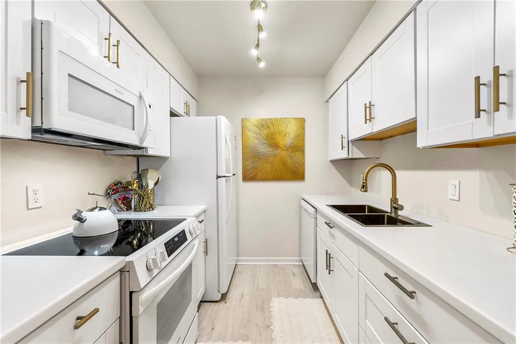 Kitchen with white appliances, light wood-type flooring, white cabinetry, and light countertops
