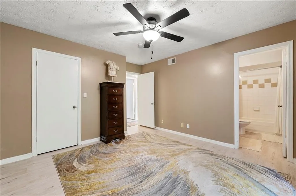 Unfurnished bedroom with a textured ceiling, light wood-style floors, ensuite bath, and a ceiling fan