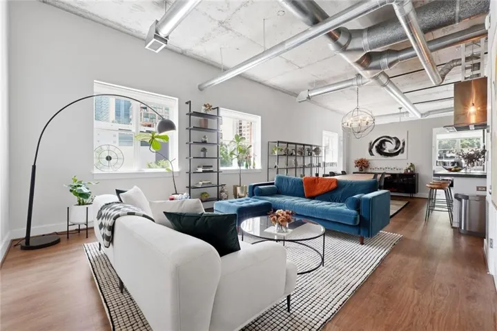 Open-concept living area featuring high ceilings with exposed ductwork, wood-finish flooring, and multiple windows