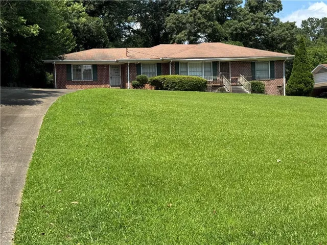 Brick exterior with green shutters, a concrete driveway, and an expansive front lawn