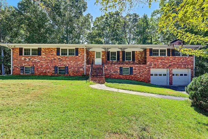 Brick exterior featuring a covered front entry with decorative ironwork, a two-car garage, and mature trees