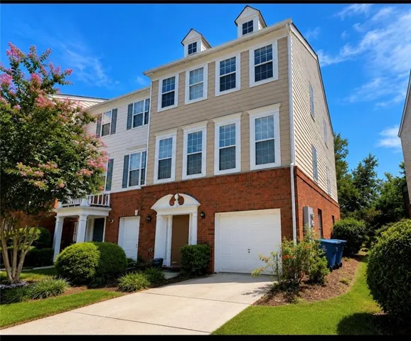Three-story townhome with brick and siding exterior, integrated garage, and dormer windows
