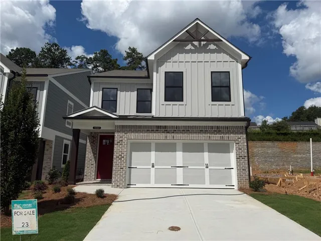Two-story exterior featuring a brick facade, vertical board-and-batten siding, black-framed windows, and an integrated two-car garage with white doors