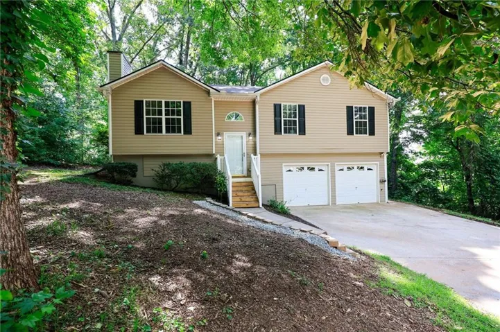 Beige exterior with black shutters, featuring a prominent two-car garage and a concrete driveway