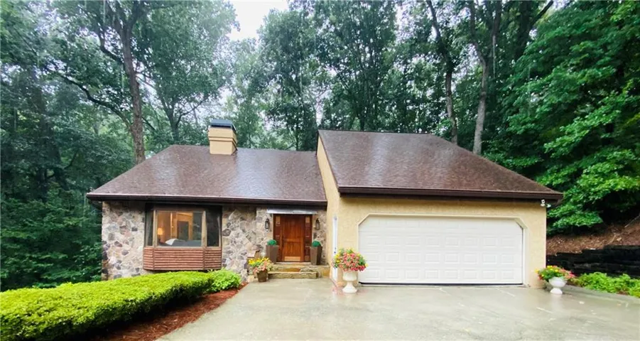 Stone facade residence with a wood front door, an integrated two-car garage, and mature landscaping