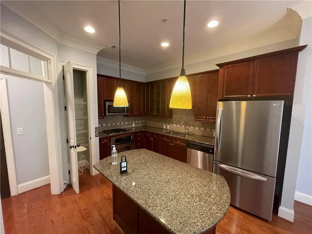 Kitchen with stainless steel appliances, dark stone counters, crown molding, light wood finished floors, and hanging light fixtures