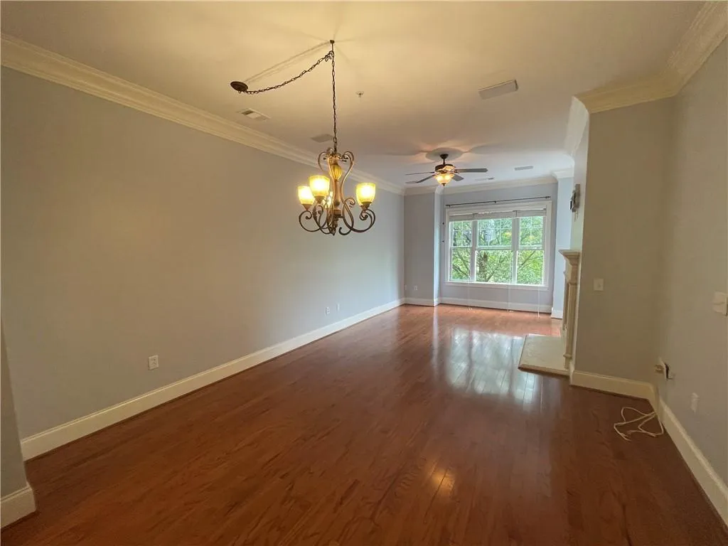 Empty room featuring a chandelier, ornamental molding, dark wood-type flooring, and a ceiling fan