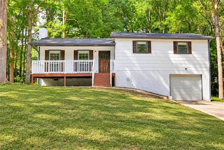 White exterior with dark wood shutters, front deck with white railing, wood-finish front door, and an integrated garage