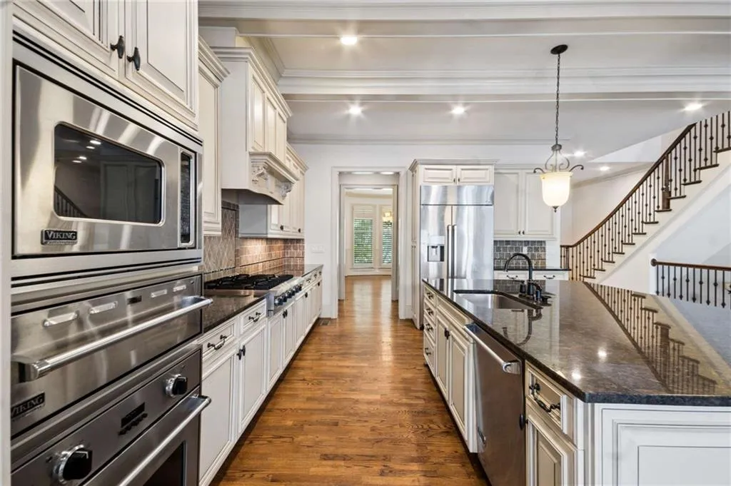 Gourmet kitchen featuring stainless steel appliances, a large central island with seating, dark stone countertops, wood-finish flooring, and white cabinetry