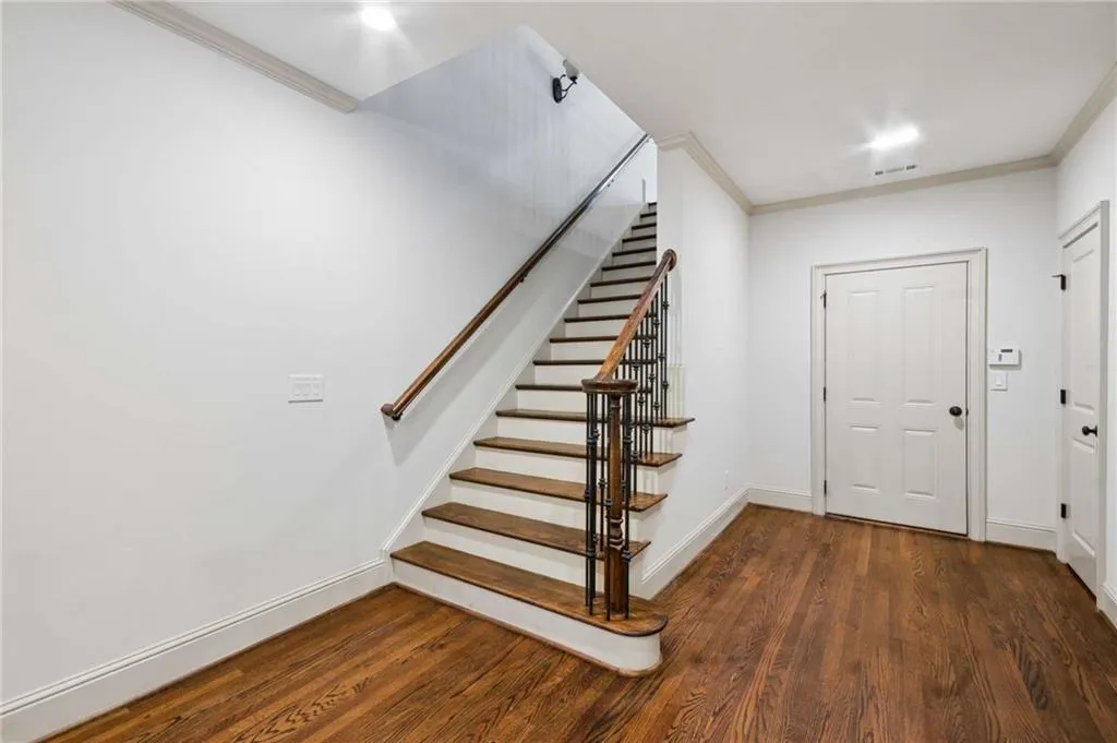Hardwood flooring, painted white walls, wood staircase with dark metal balusters, crown molding, and recessed lighting