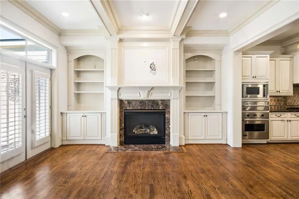 Hardwood flooring throughout featuring a fireplace with a stone surround, built-in cabinetry, and integrated shelving