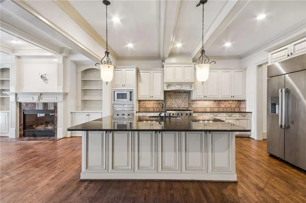 Spacious kitchen featuring an island with a dark countertop, white cabinetry, stainless steel appliances, and wood-finish flooring