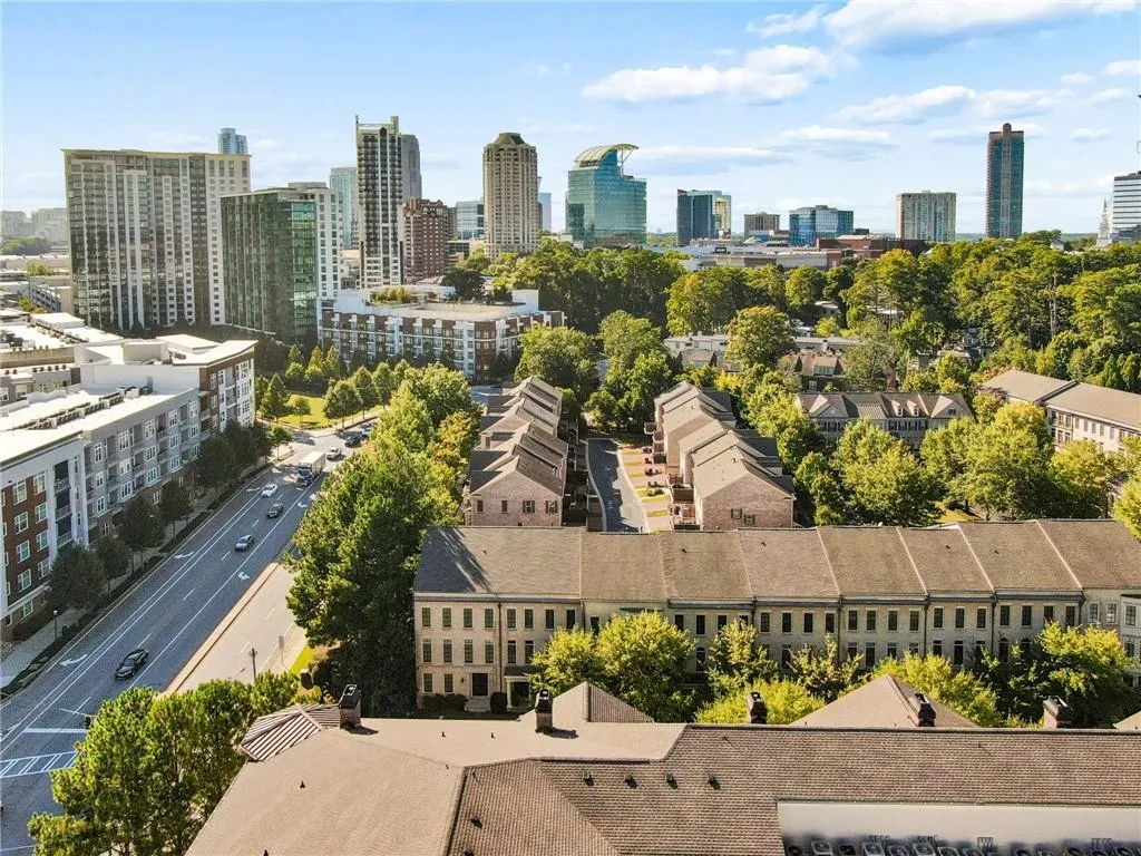 Urban landscape featuring mature trees, high-rise buildings, multi-story residential structures, and a clear sky backdrop