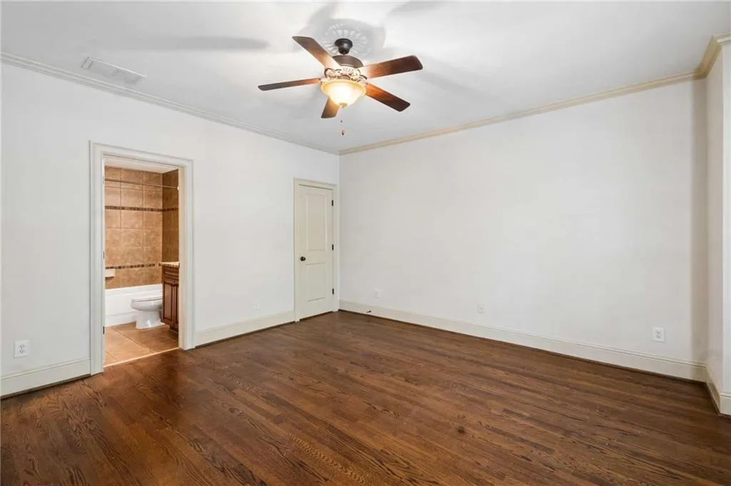 Hardwood flooring, ceiling fan with light fixture, crown molding, and an attached bathroom with tiled flooring