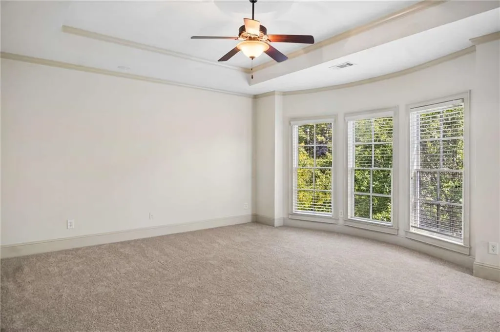 Tray ceiling with a ceiling fan, three large windows, and wall-to-wall carpeting