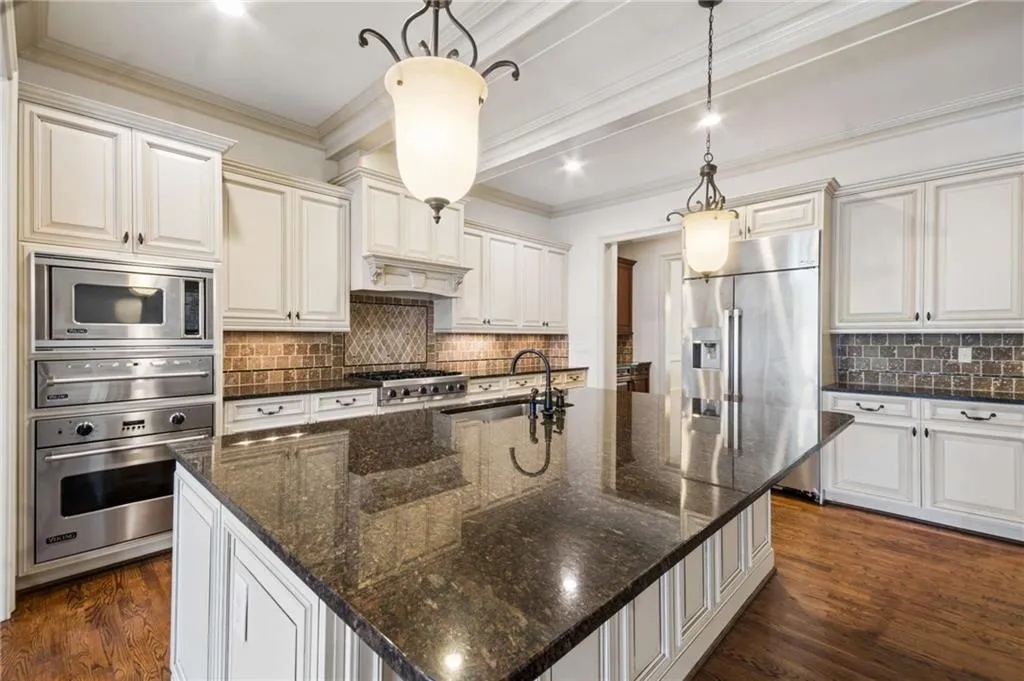 Spacious kitchen featuring an expansive center island, paneled cabinetry, stainless steel appliances, and wood-finish flooring