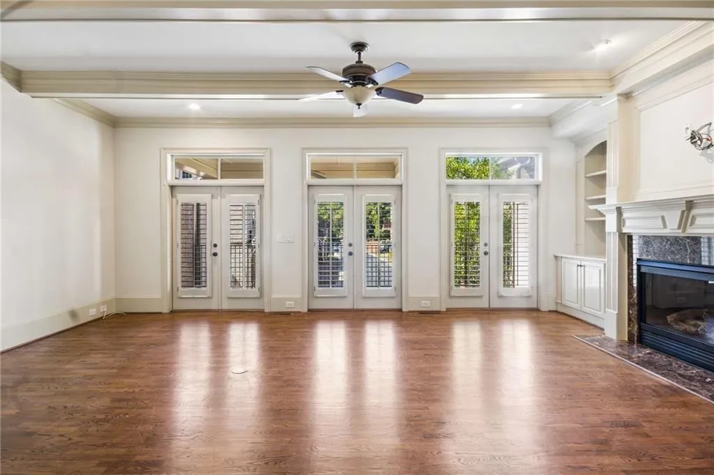 Wood-finish flooring, three sets of double French doors with transom windows, built-in shelving, a built-in fireplace, and a ceiling fan with integrated lighting