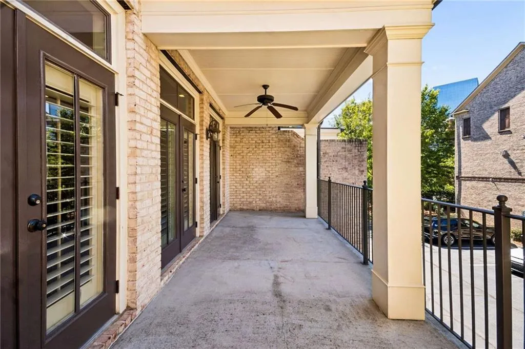 Covered outdoor balcony featuring a ceiling fan, brick exterior, and dark-framed doors with transoms
