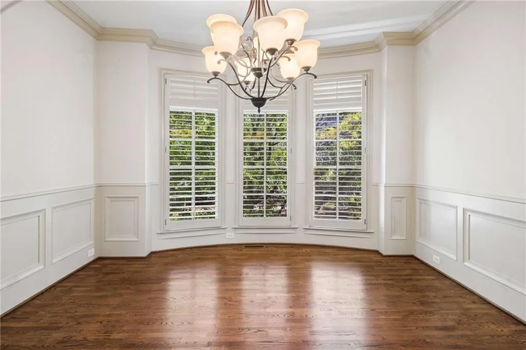 Curved bay window, crown molding, wainscoting, wood-finish flooring, and a multi-arm chandelier