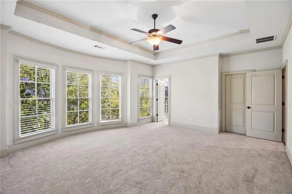 Tray ceiling with a ceiling fan, light-toned carpeting, multiple windows, and panel doors