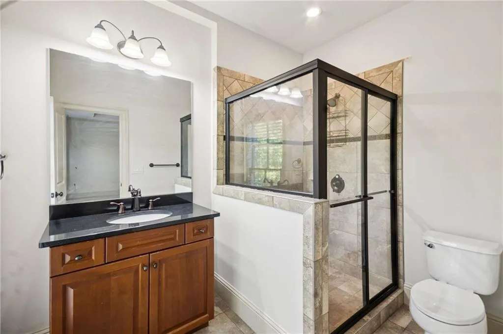 Vanity with a dark countertop and undermount sink, wood-finish cabinetry, and an oversized mirror