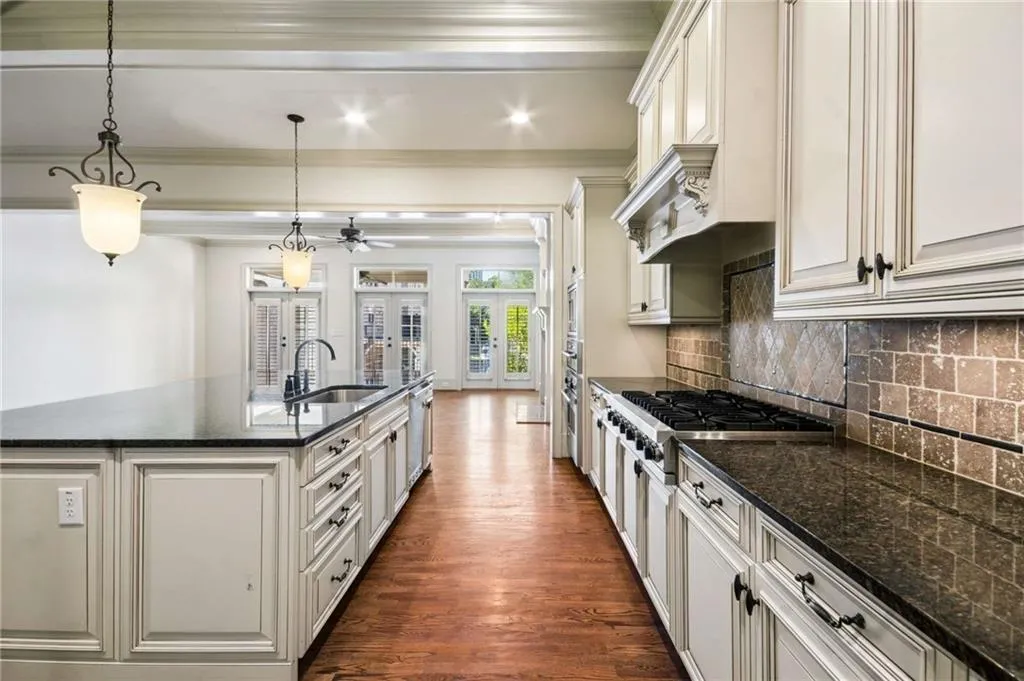 Kitchen featuring an expansive island with a built-in sink, white cabinetry with dark hardware, dark countertops, and a tiled backsplash
