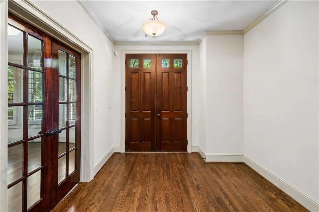Rich wood-finish flooring, paneled entry doors, transom window detailing, double French doors, and crown molding