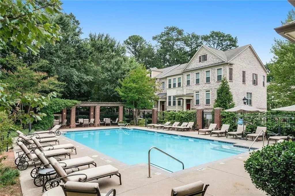 Community swimming pool with concrete decking, surrounding brick buildings, and a pergola-covered seating area