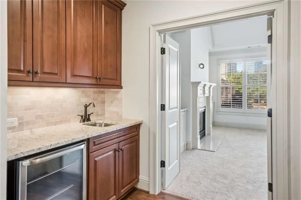 Integrated wet bar featuring wood cabinetry, stone-finish countertop, under-cabinet lighting, and a beverage refrigerator