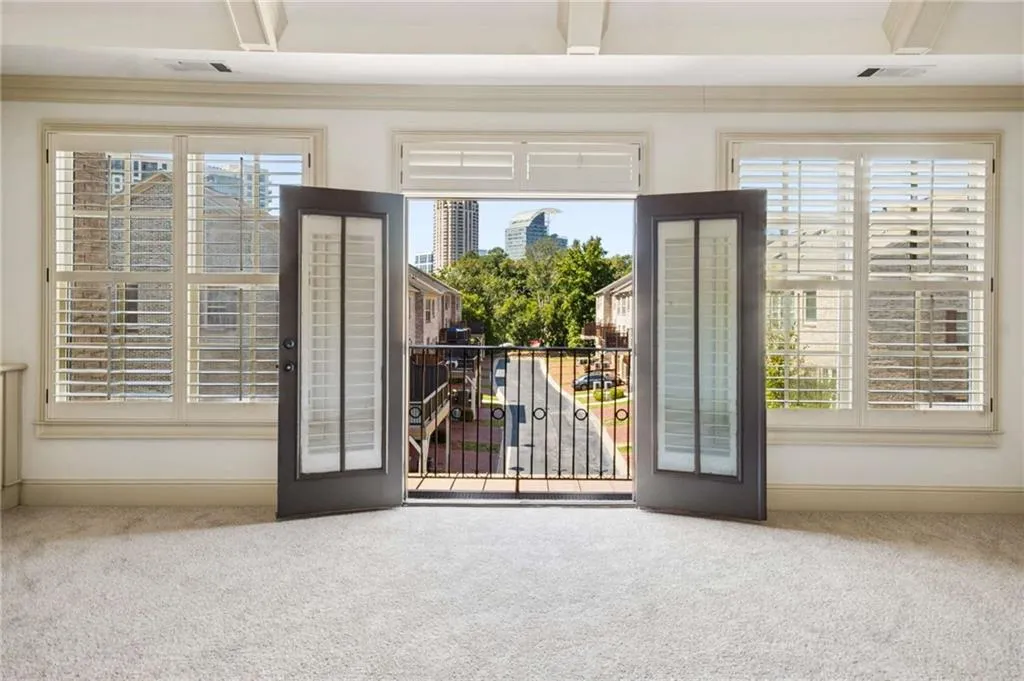 Carpeted room with a balcony, double doors, and two windows featuring plantation shutters