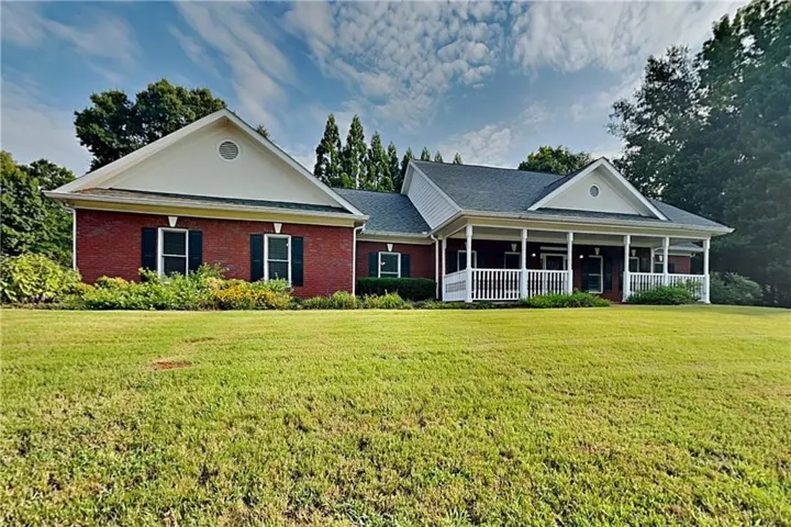 Brick ranch-style residence featuring a prominent covered front porch with white railing