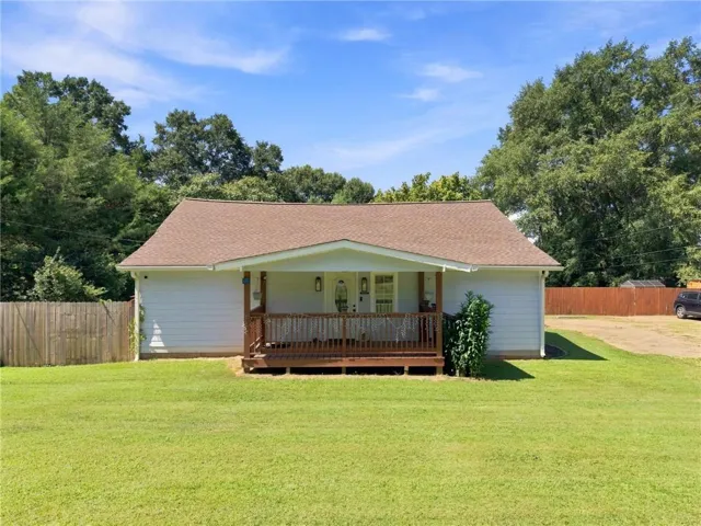 White siding exterior with a brown shingle roof, complemented by a wood-finish front porch and railing