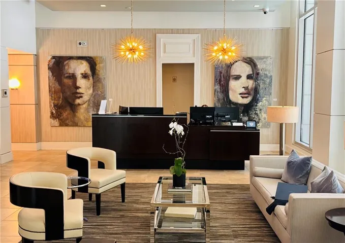 Welcoming lobby area featuring a dark wood reception desk, two spherical gold-tone chandeliers, textured wall coverings, and tile flooring