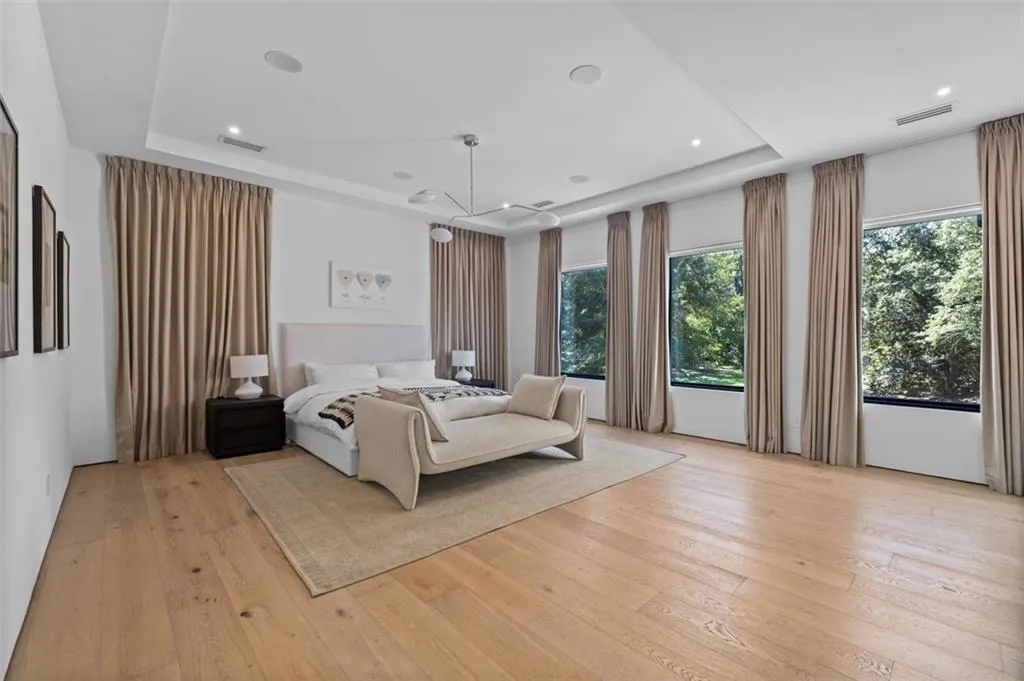 Graciously sized, this retreat features space for sitting area, white oak floors, a tray ceiling with recessed lighting, and five large windows that fill the space with natural light. The suite includes a custom oversized closet and an en suite bath with custom lighting, combining luxury and comfort in one elegant space.