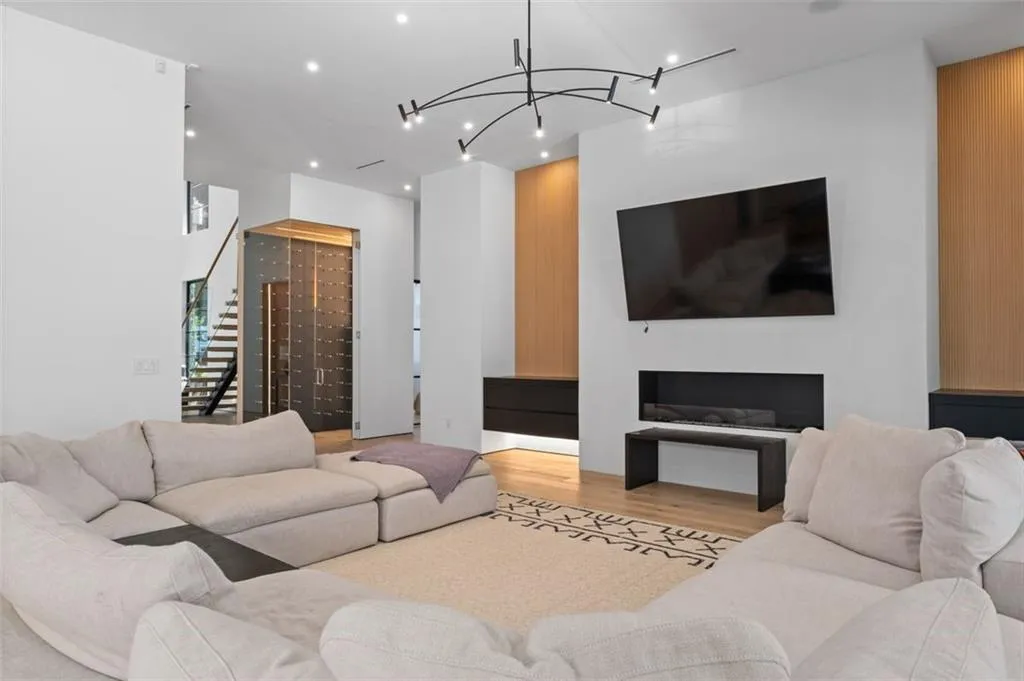 Located just off the kitchen, this inviting space features 12-foot ceilings, white oak floors, a sleek modern linear fireplace, striking Moooi lighting, and built-in drawers. Oversized sliding glass doors and expansive windows frame picturesque views of the resort-style backyard, seamlessly blending indoor and outdoor living.