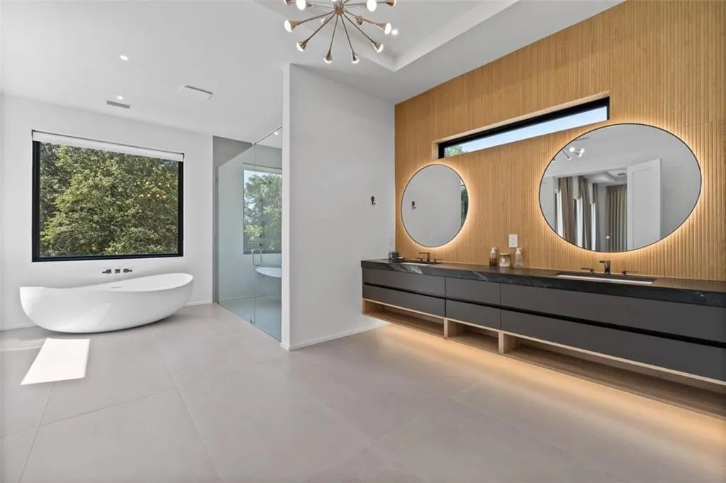 Luxuriously appointed, this spa-like retreat features an oversized custom vanity with lighted mirrors, a seamless oversized shower, a soaking tub, and two picture windows that fill the space with natural light.