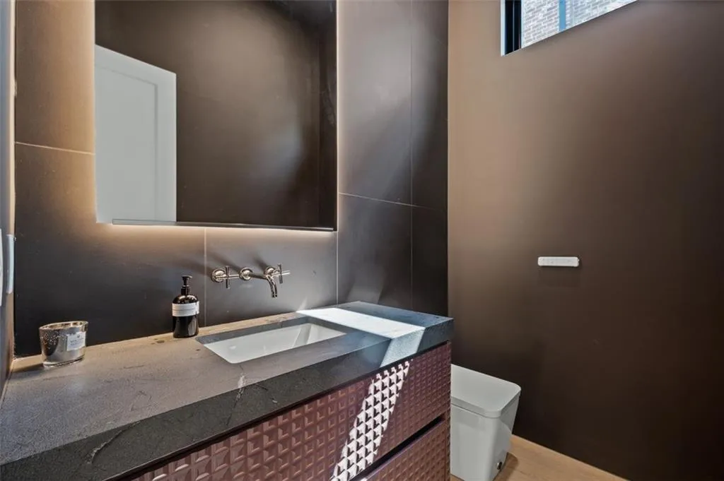 Boasting 12-foot ceilings, white oak flooring, a custom vanity with bespoke lighting, and a smart toilet, this stylish half bath combines modern convenience with elegant design.