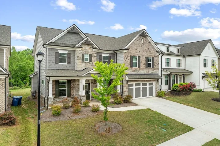 Multi-story exterior featuring a stone and siding facade, a covered front porch, an attached garage with a driveway, and a landscaped front yard