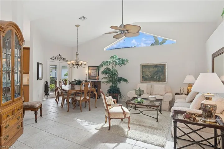 Living room with light tile patterned floors, high vaulted ceiling, a healthy amount of sunlight, and ceiling fan with notable chandelier
