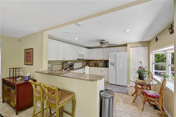 Kitchen featuring light tile flooring, kitchen peninsula, tasteful backsplash, white cabinets, and white appliances