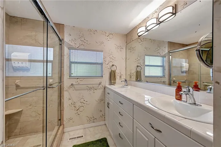Bathroom with tile floors, vanity with extensive cabinet space, an enclosed shower, and double sink