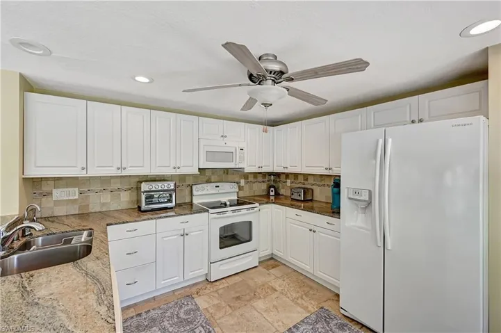 Kitchen featuring tasteful backsplash, white appliances, light tile floors, sink, and white cabinetry