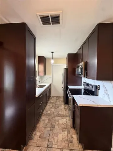 Galley kitchen featuring dark wood cabinetry, white countertops with veining, stainless steel appliances, and stone-look tile flooring