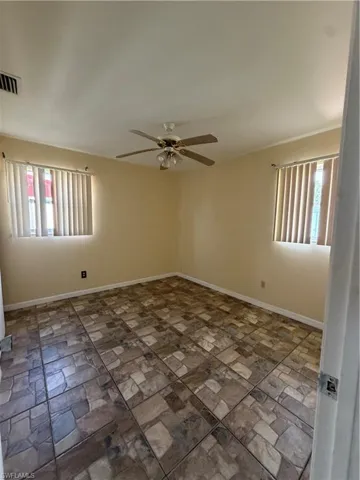 Bedroom featuring patterned tile flooring, two windows with vertical blinds, a ceiling fan with integrated lighting, and light-toned wall paint
